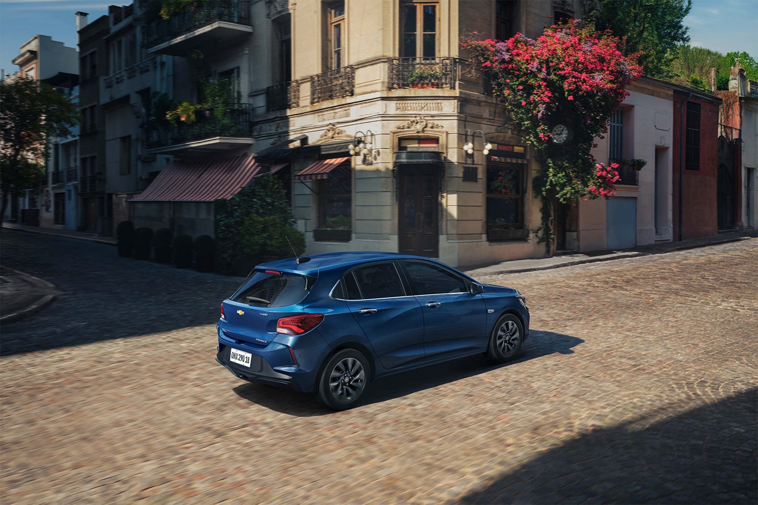 Vista trasera del Chevrolet Onix Hatchback azul en una calle urbana empedrada